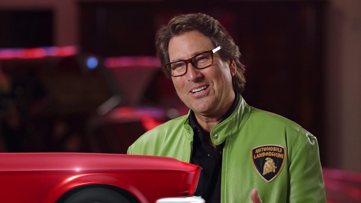 Man in a green Lamborghini jacket beside a red Lamborghini.